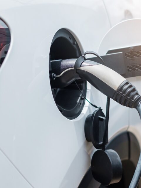 White electric car charging at a station, close-up of the plugged-in cable and rear tail light