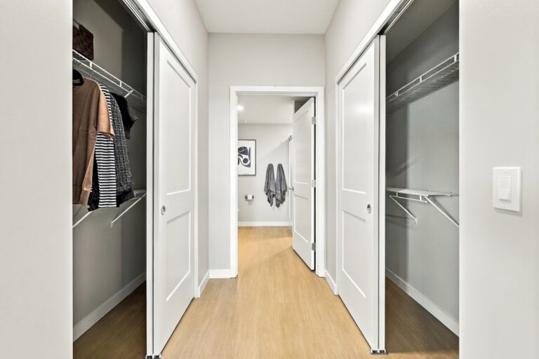 Walk-in closet with double-sided shelving, hanging clothes, and sliding doors in a Bob Apartments unit