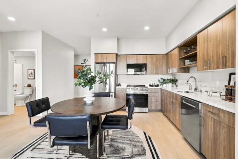 Modern Bob Apartments kitchen with wood cabinetry, stainless steel appliances, white countertops, and a round dining table with black chairs
