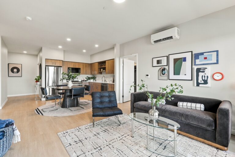 Open-plan Bob Apartments living room and kitchen with modern furnishings, wood cabinetry, stainless-steel appliances, and wall art