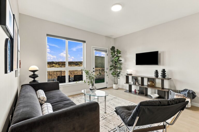 Modern living room in a Bob Apartments unit, featuring a sofa, glass coffee table, wall-mounted TV, and balcony access