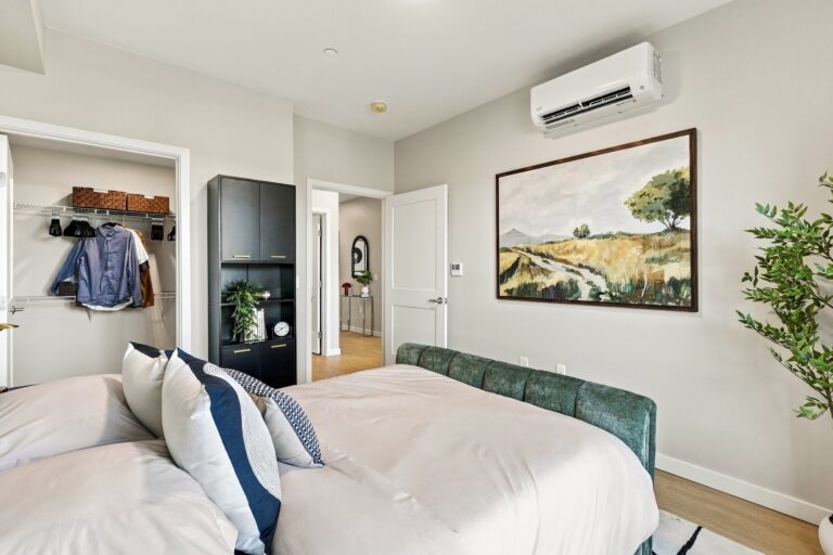 Bob Apartments bedroom with a green upholstered bed, walk-in closet, built-in storage, wall-mounted air conditioner, and landscape artwork