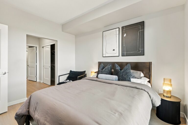 Staged bedroom in a Bob Apartments unit with a king bed, walk-in closet, nightstand, and modern wall art